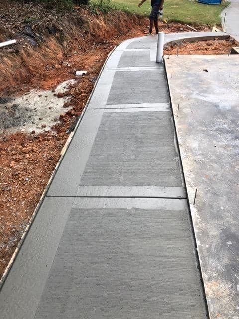 Freshly poured concrete sidewalk with a textured finish bordering a construction site.