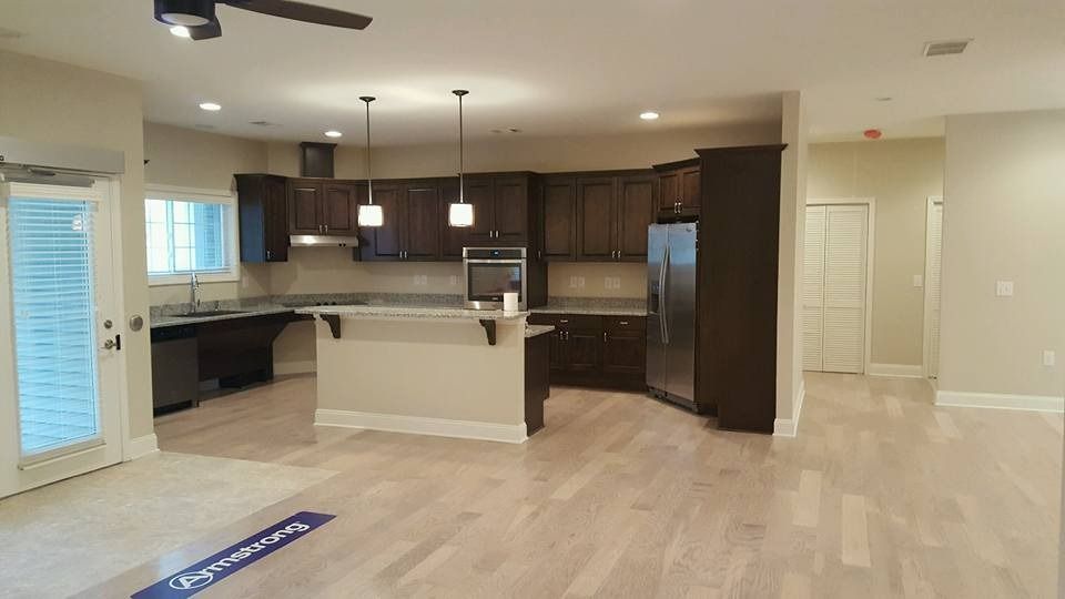 Open-concept kitchen with dark wood cabinets, stainless steel appliances, a center island, and light hardwood floors.