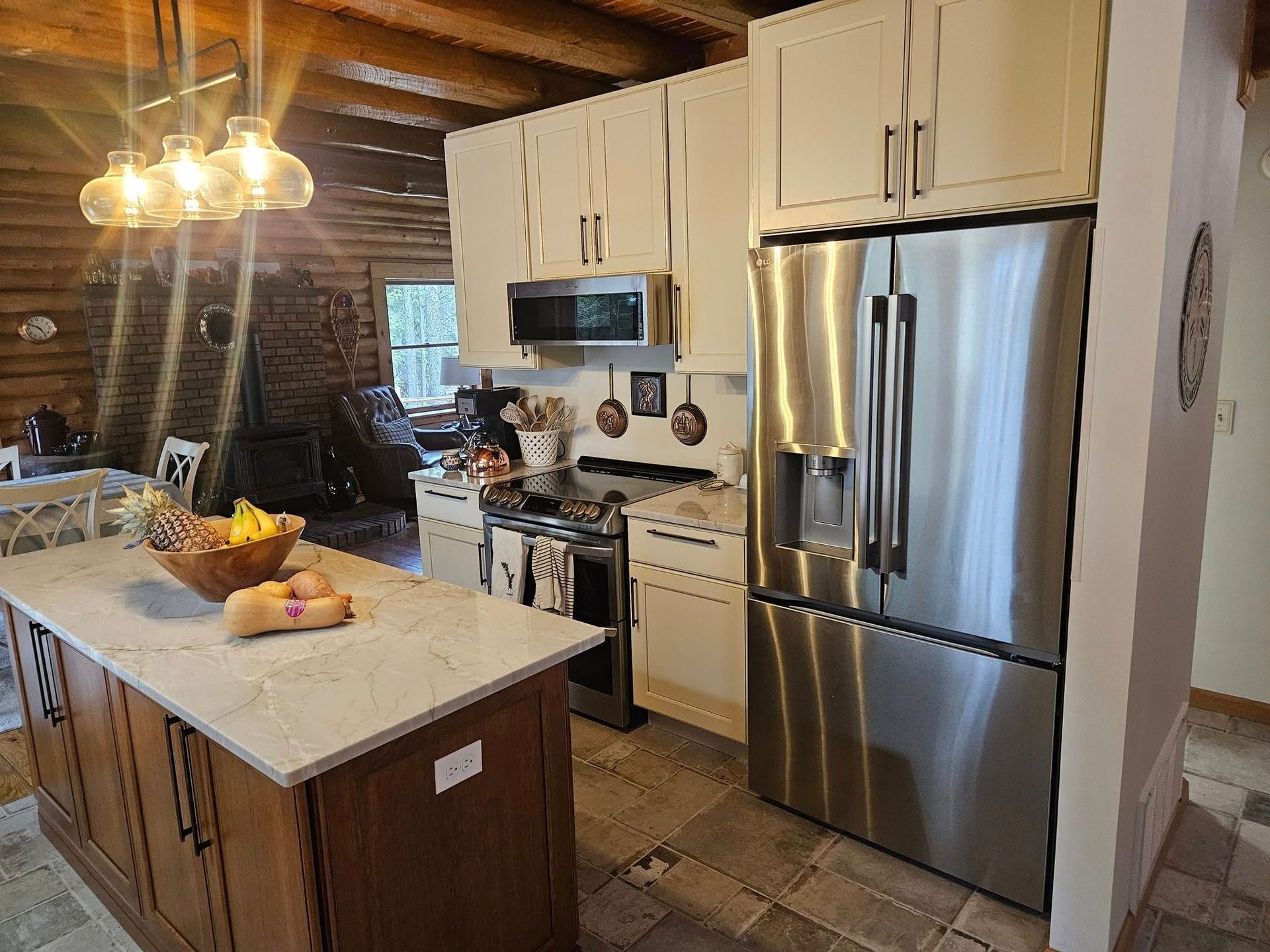 A rustic kitchen with wood-paneled walls, an island, white cabinets, and stainless steel appliances.