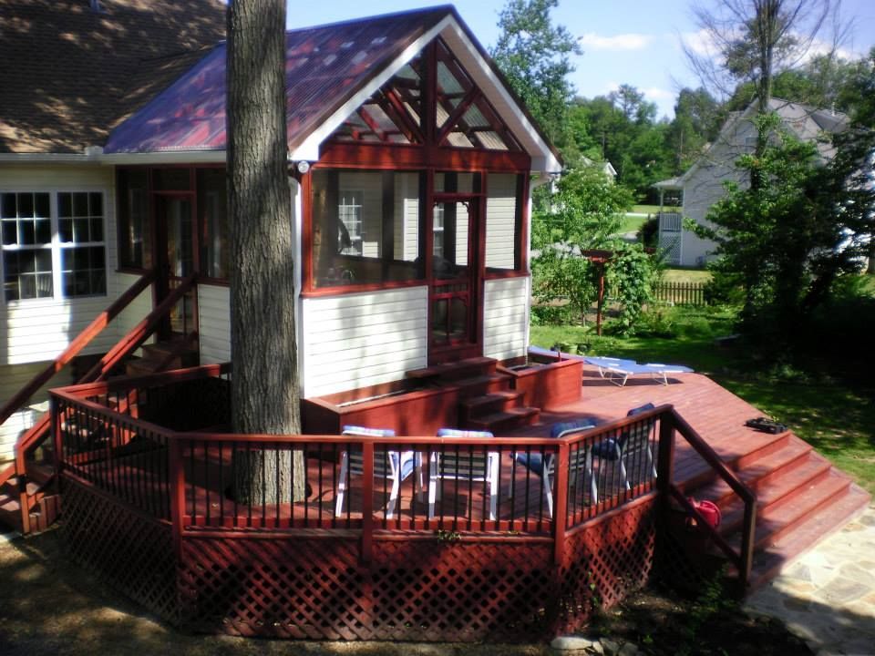 A screened-in porch with a red-painted wooden deck built around a tree, with outdoor furniture on a sunny day.