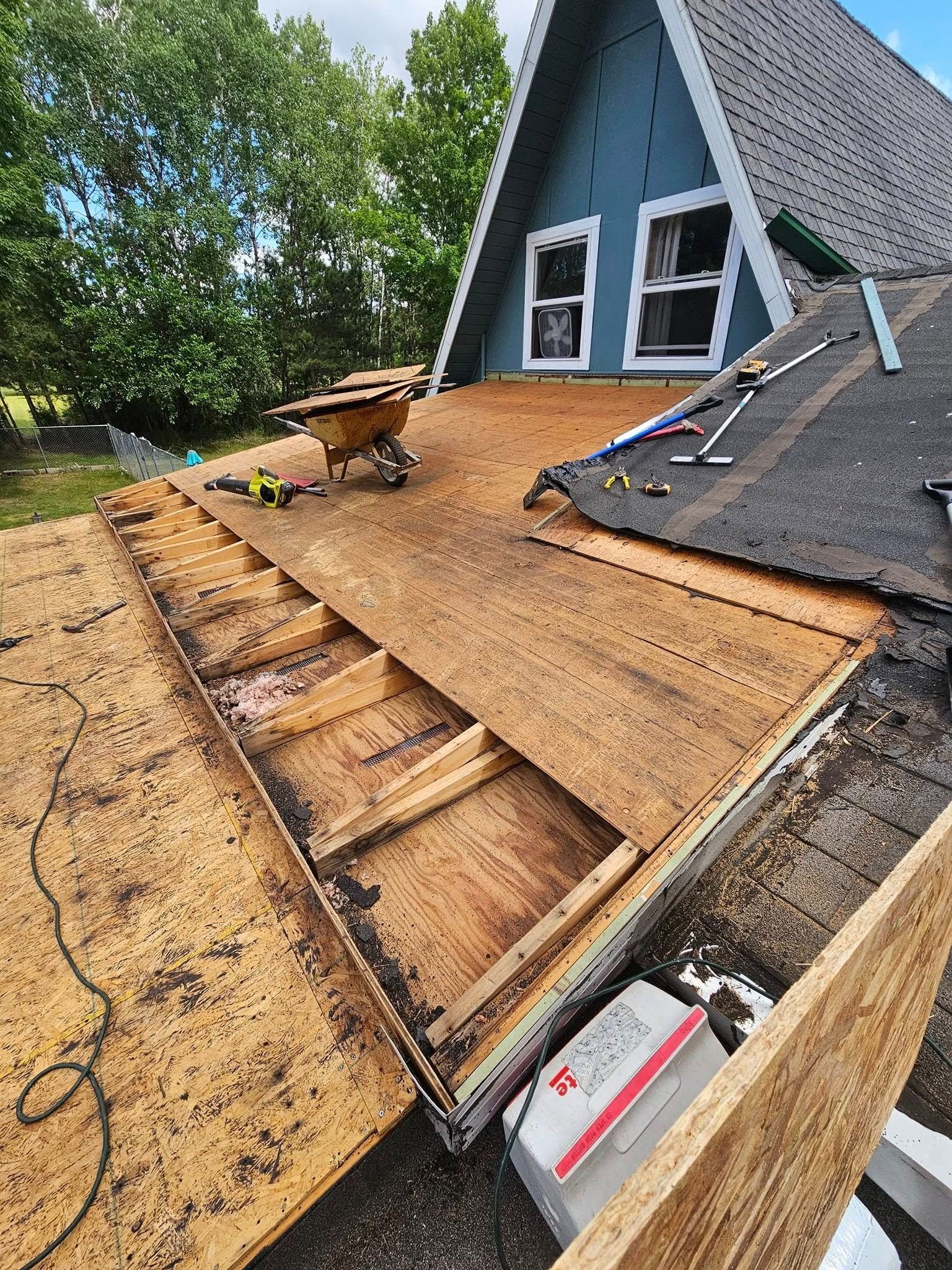 A blue A-frame house undergoing roof repair with partially removed plywood decking exposing the rafters.