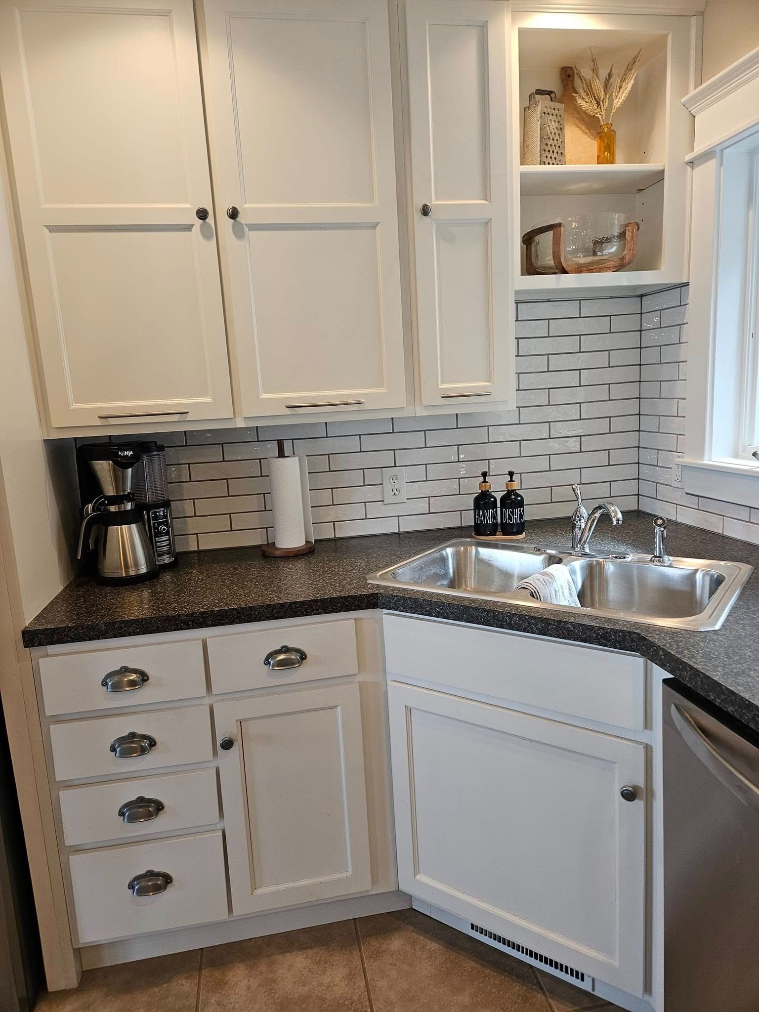 White kitchen cabinets with black speckled countertops, a double-basin stainless steel sink, and patterned backsplash.