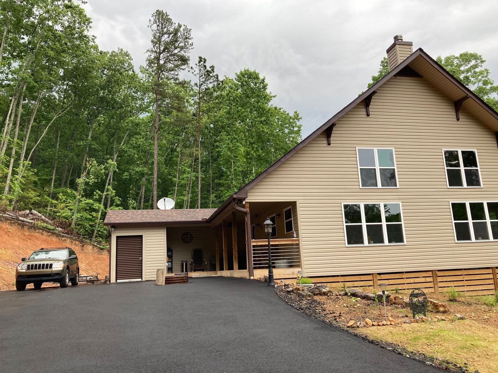Tan-sided house exterior with large white-framed windows, wood lattice skirting, and an American flag on the porch.