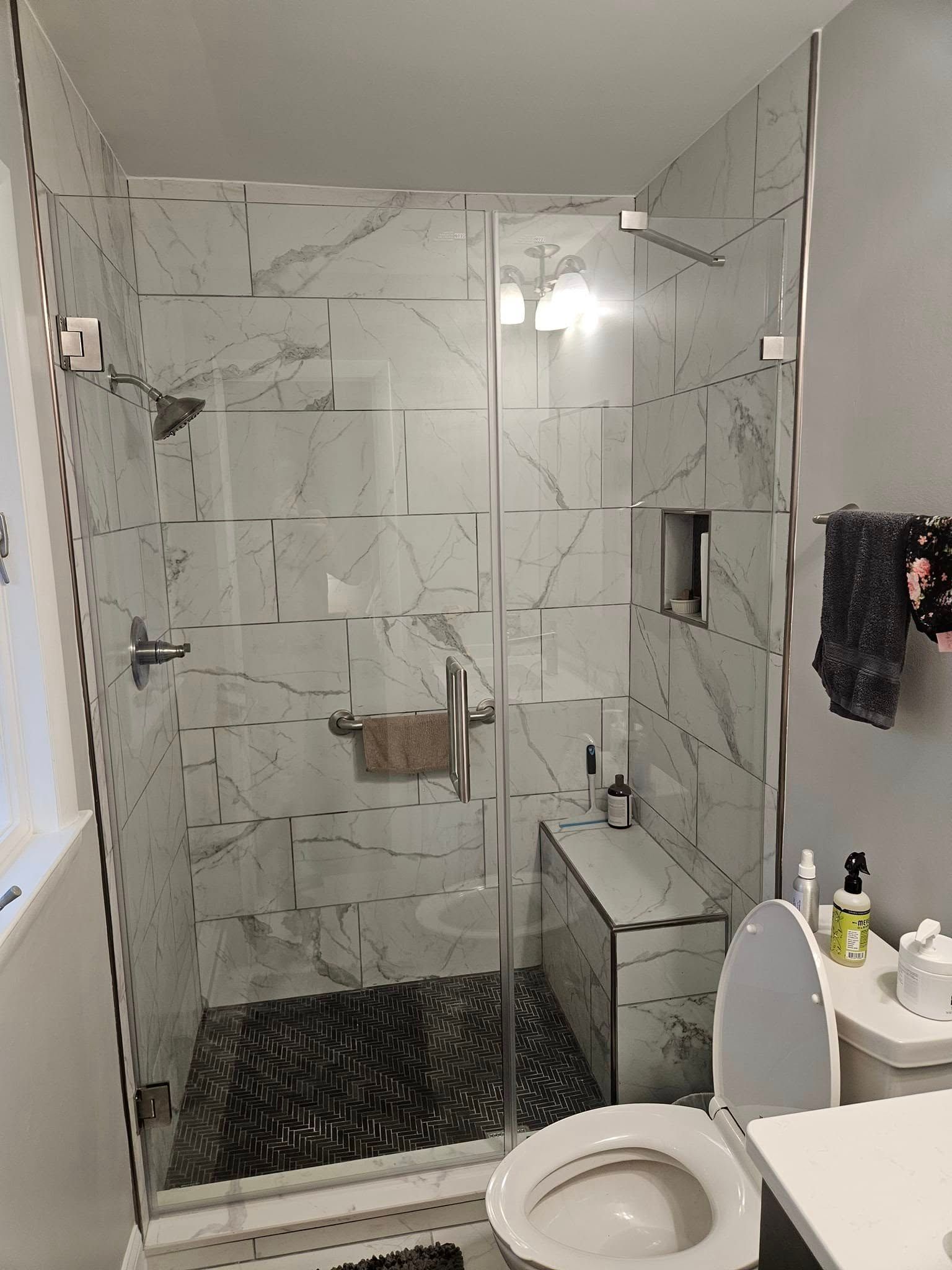 A small bathroom with a vanity, toilet, and walk-in shower with marble-look walls, viewed through an open doorway.
