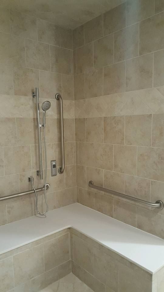 A beige tiled walk-in shower featuring a white built-in bench, a handheld showerhead, and stainless steel grab bars.