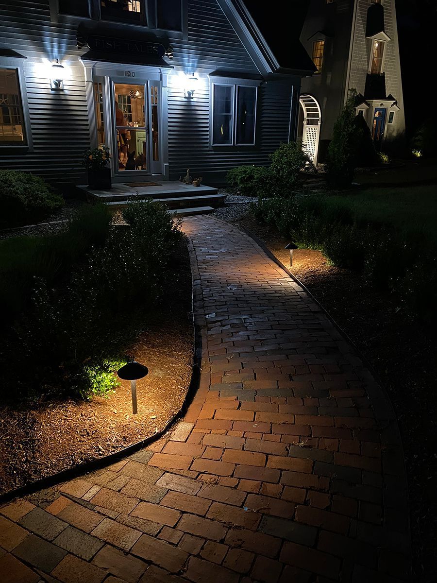 A brick walkway illuminated by small pathway lights leads to the front entrance of a house at night.