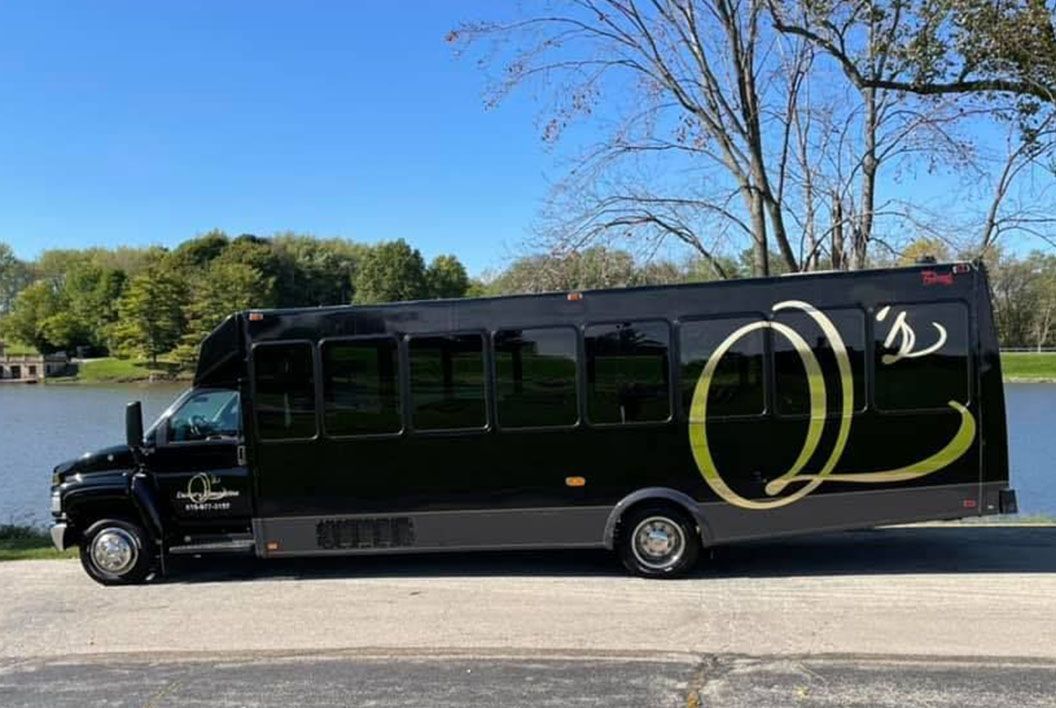 A black bus is parked on the side of the road next to a body of water.