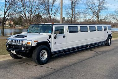 A white hummer limousine is parked on the side of the road.