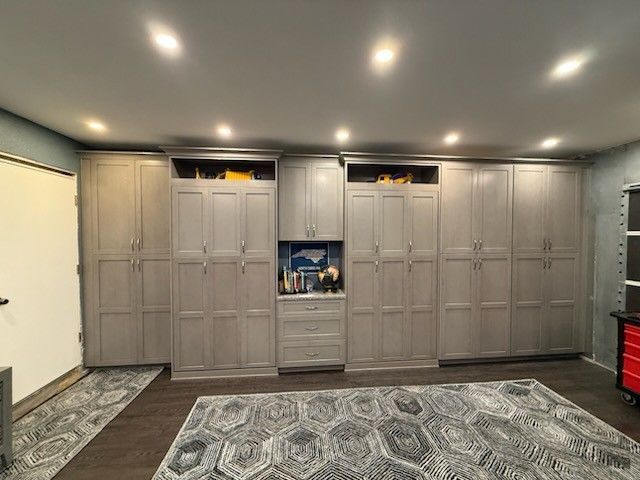 Gray storage cabinets line a garage wall, with overhead lighting. A decorative rug covers the floor.