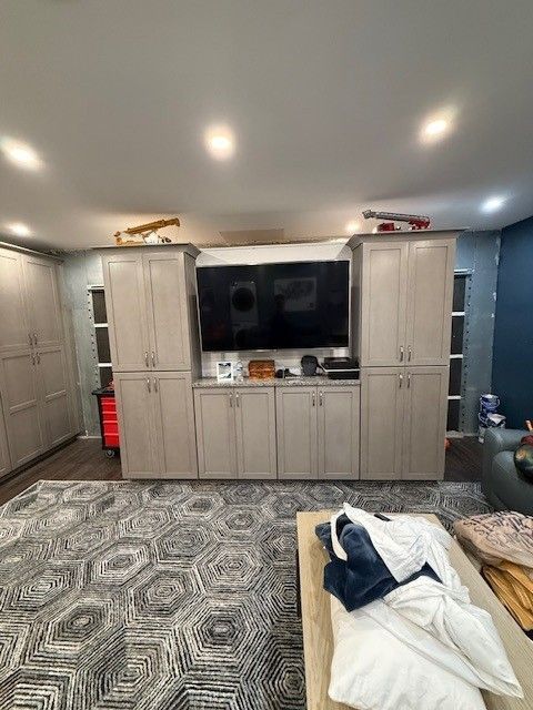 Built-in light gray cabinets with a TV in the center, a patterned rug, and a light-colored coffee table.