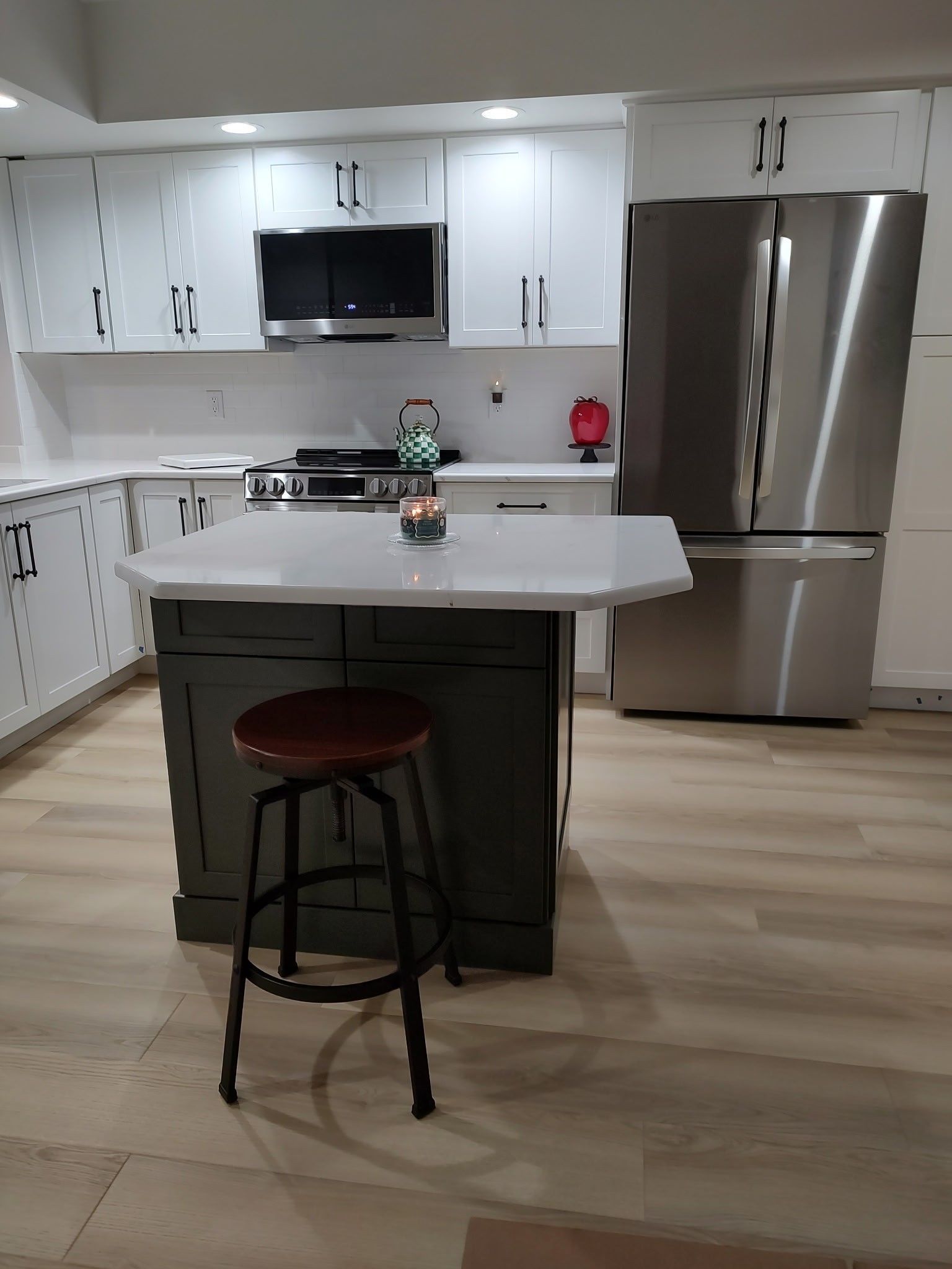 Modern kitchen with white cabinets, dark island, stainless steel fridge, and wood stool.