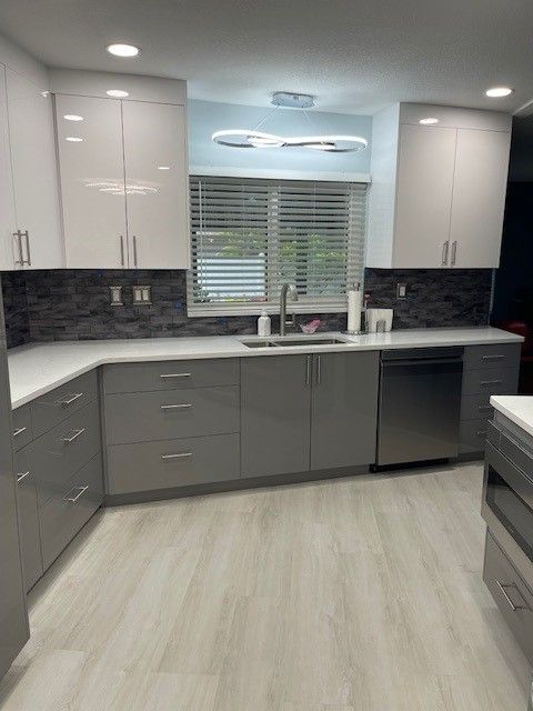 Modern kitchen with gray and white cabinets, stainless steel appliances, and white countertops.