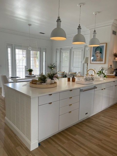 White kitchen island with three pendant lights and built-in appliances.
