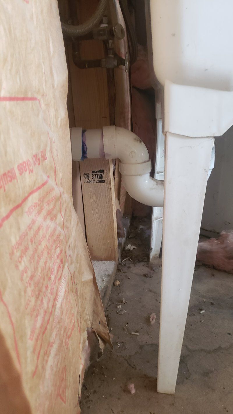 A white sink is sitting next to a wall with pipes coming out of it.