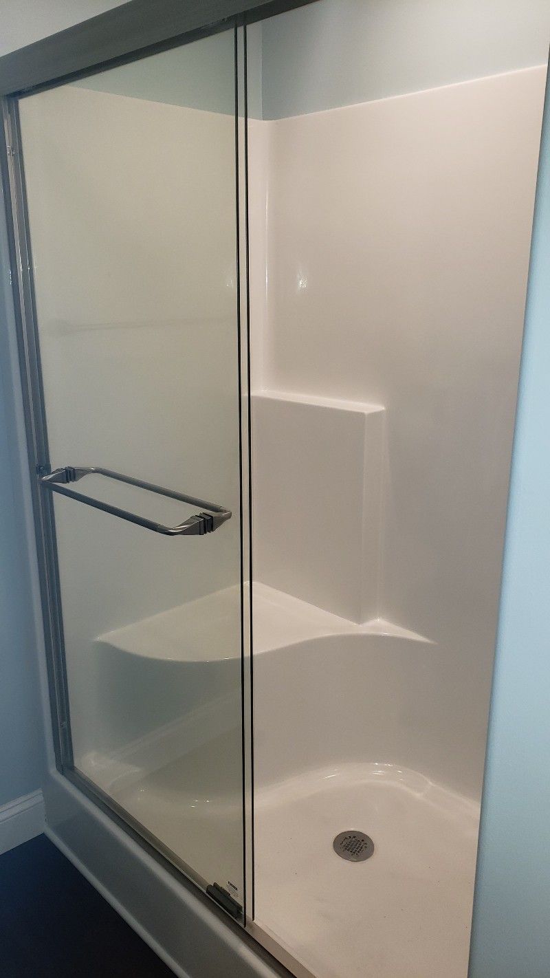 A shower stall with a sliding glass door and a seat.