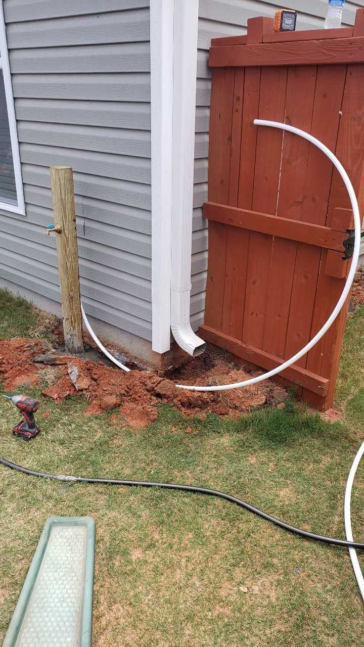 A hose is laying on the ground next to a fence and a house.