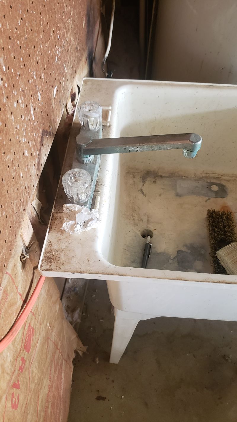 A white sink with a faucet and a brush on it is sitting next to a wall.
