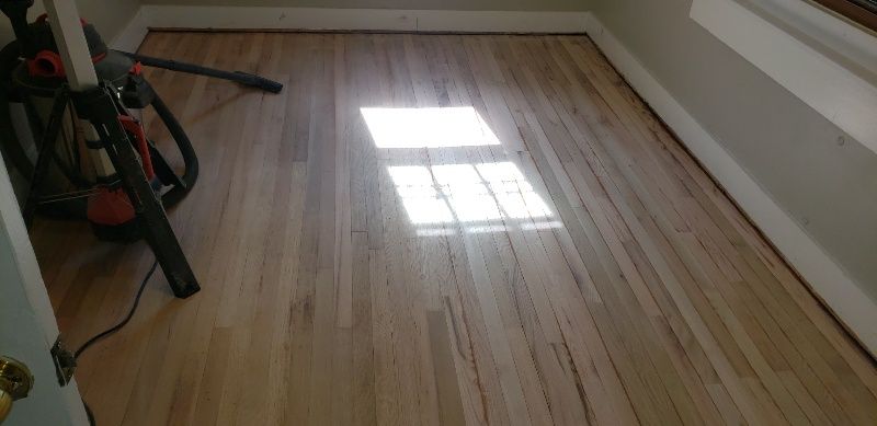 A wooden floor in a room with a window and a vacuum cleaner.