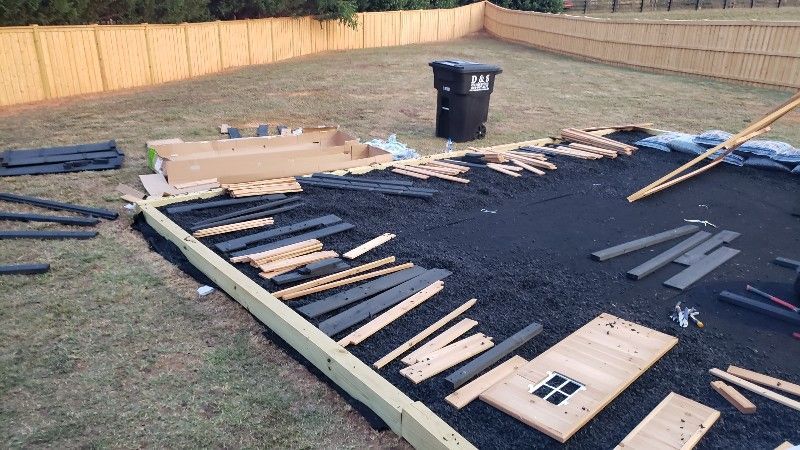 A pile of wood is laying on the ground in a backyard.