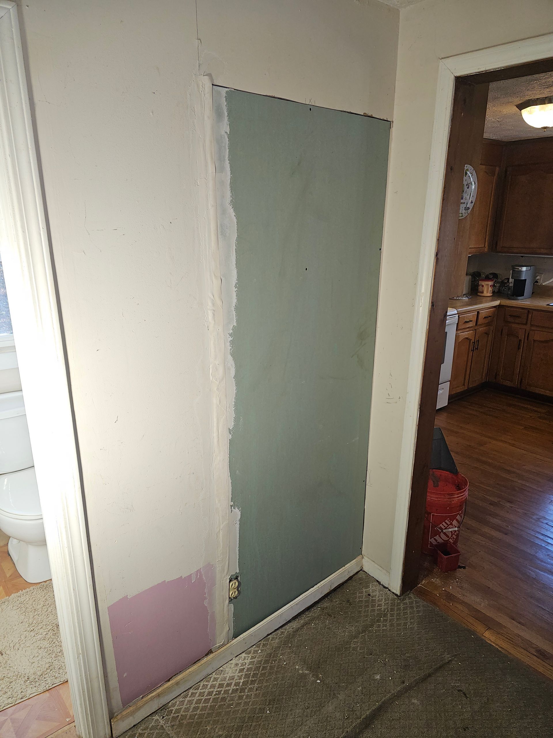 Gray drywall sheet installed on a wall; doorway and bathroom visible.