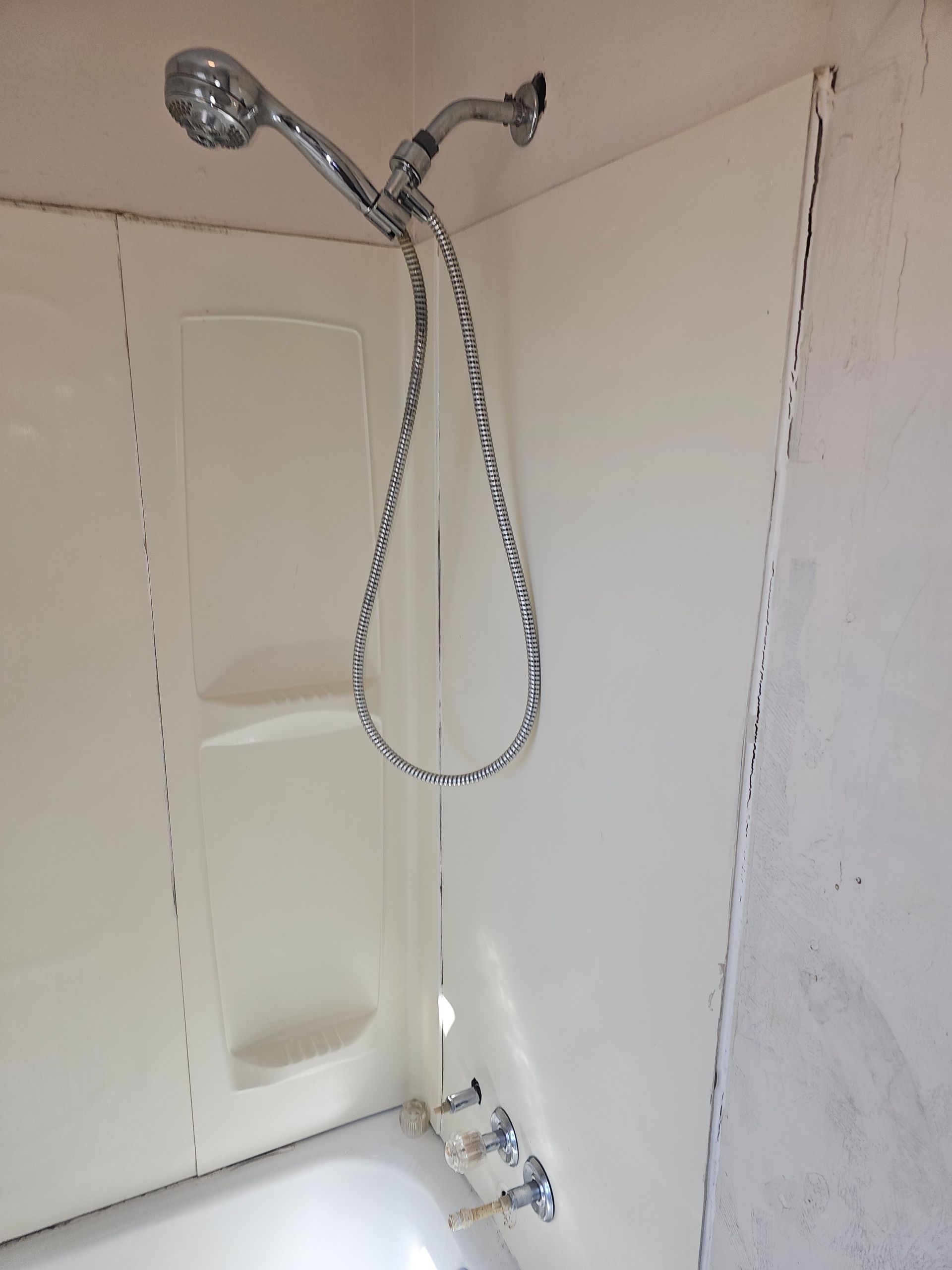 White shower stall with handheld showerhead over a bathtub.