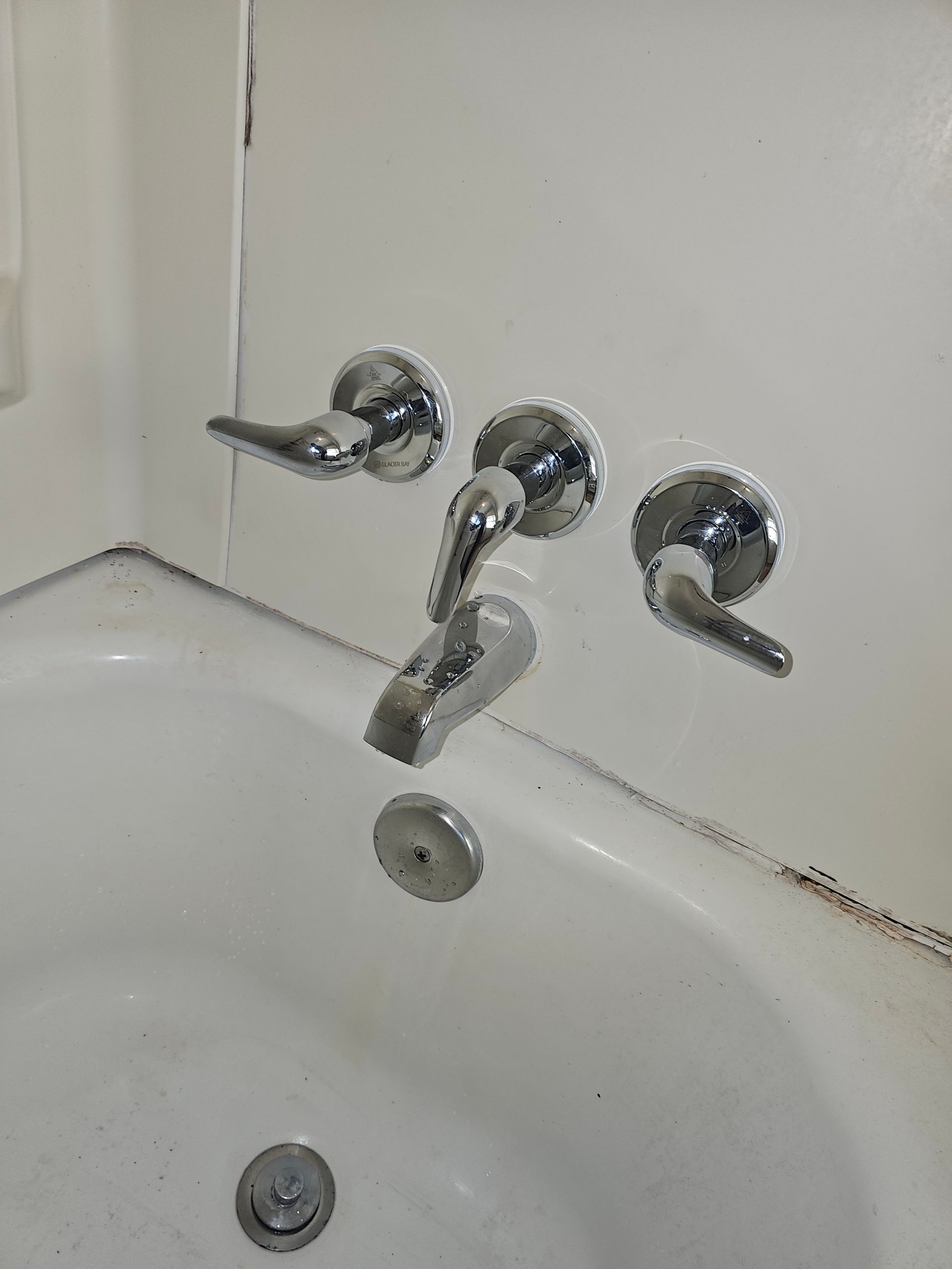 Bathtub with three chrome faucet handles and a spout, positioned against a white wall.