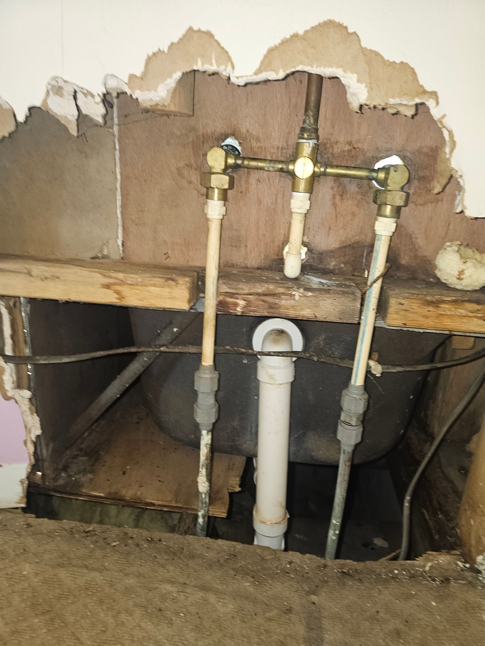 Plumbing fixtures with exposed pipes and drain, set in a wall cavity, with a visible bathtub.