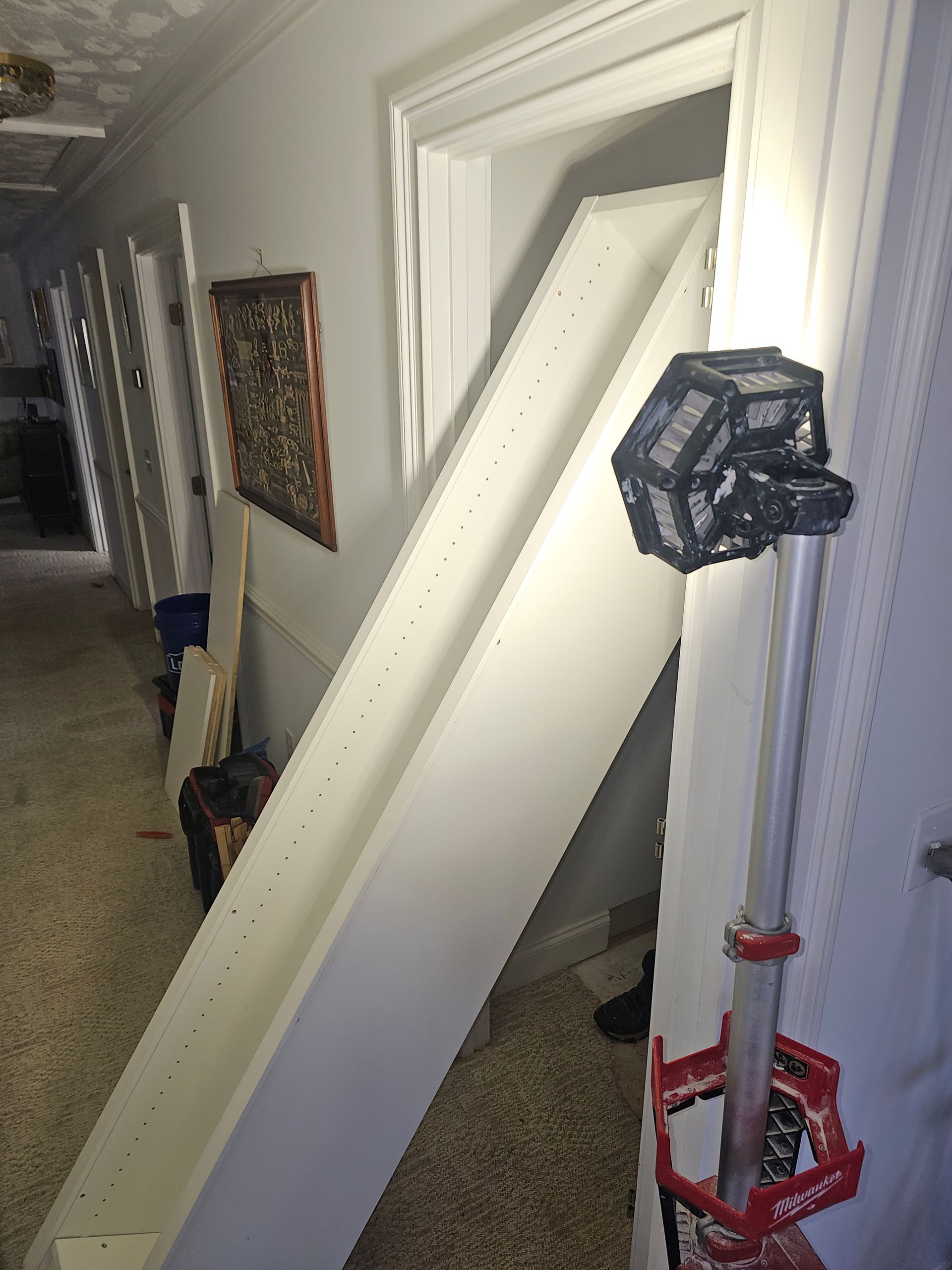 Long white shelf propped up in a hallway, leaning against a doorway. A light is positioned next to it.