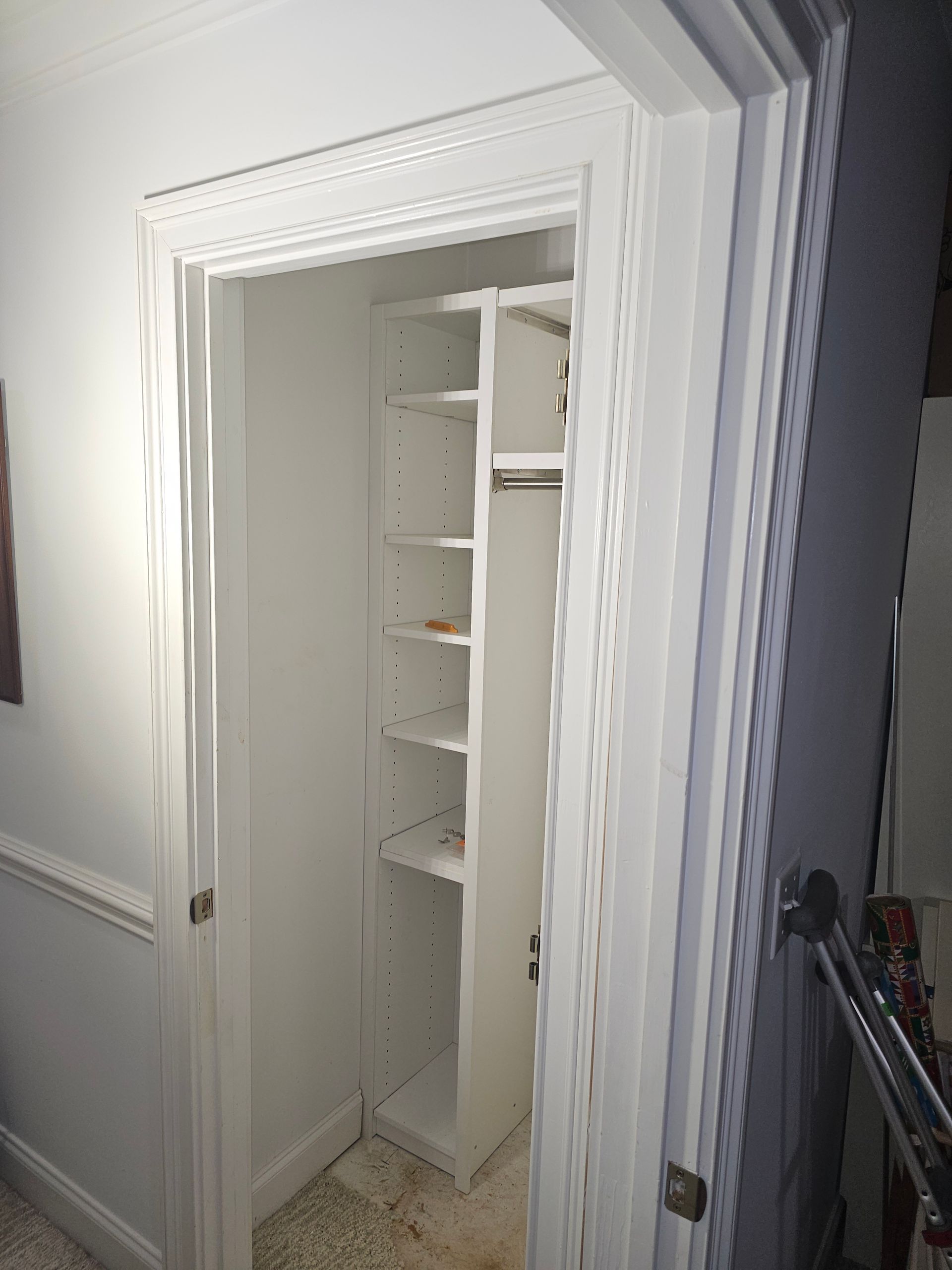 White closet with shelves and a hanging rod, viewed through a white door frame.