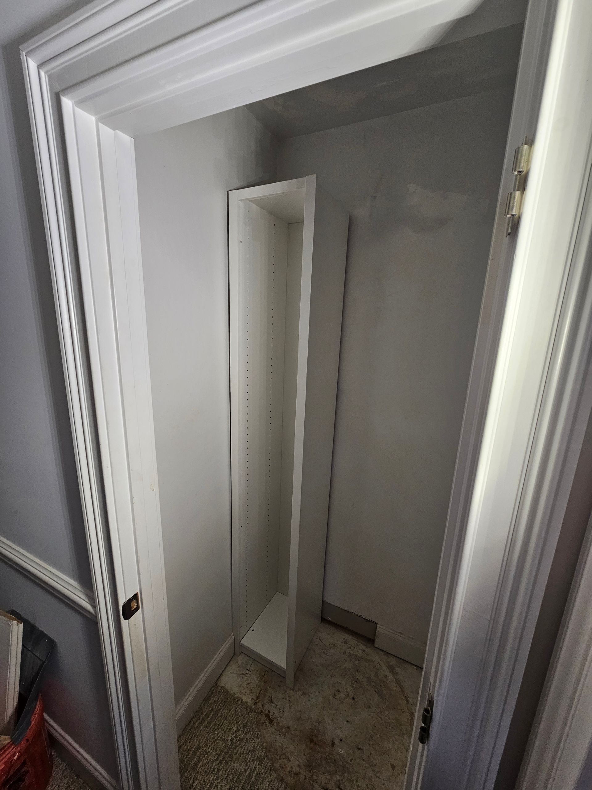 Narrow closet with tall, white shelving unit. White door slightly open at the back.