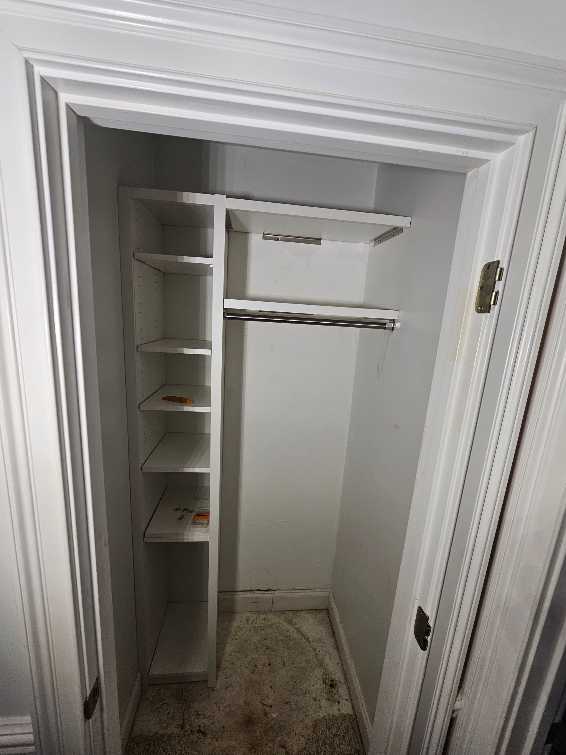 Empty white closet with built-in shelving and clothes rod. Dirty floor visible.