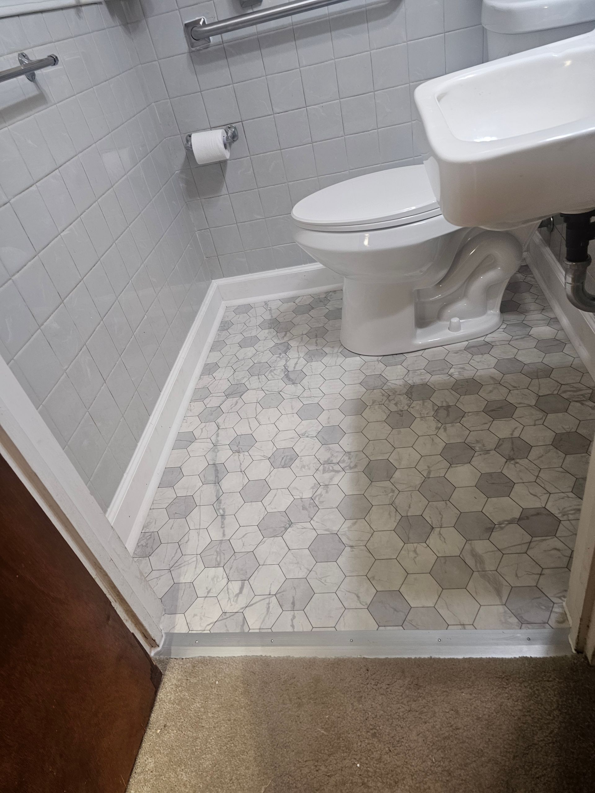 Small bathroom with gray hexagon floor tiles, white toilet, and gray wall tiles.