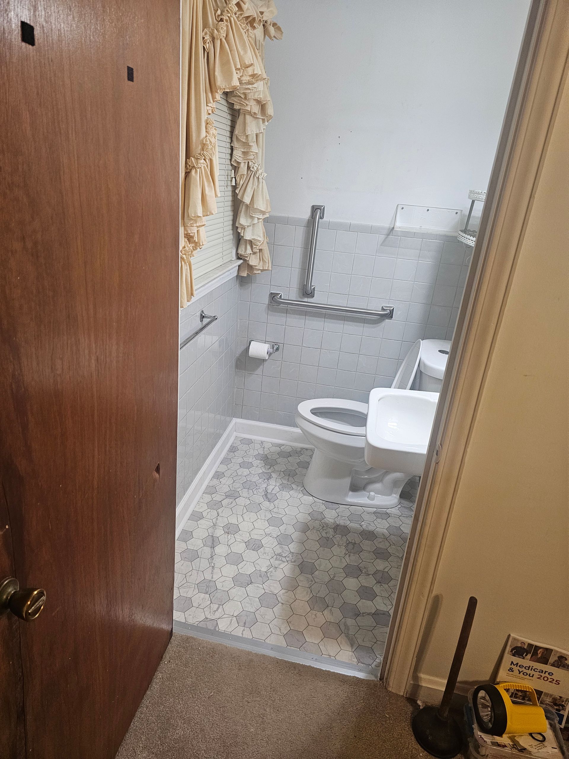 Bathroom with toilet, grab bar, patterned tiles, and partly open door.