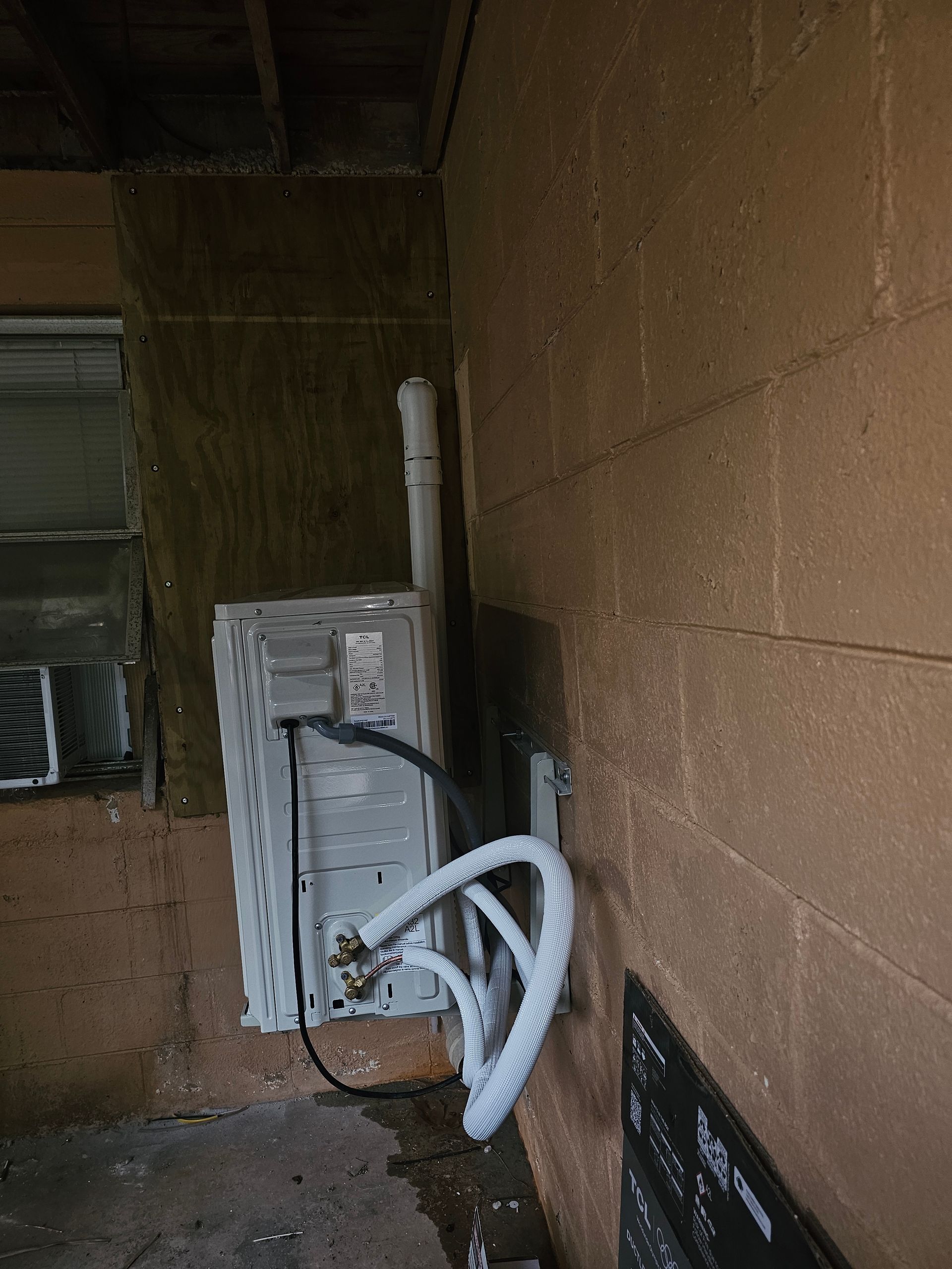 Utility area with white electrical conduit, wall-mounted panel, and coiled hoses against tan cinderblock walls