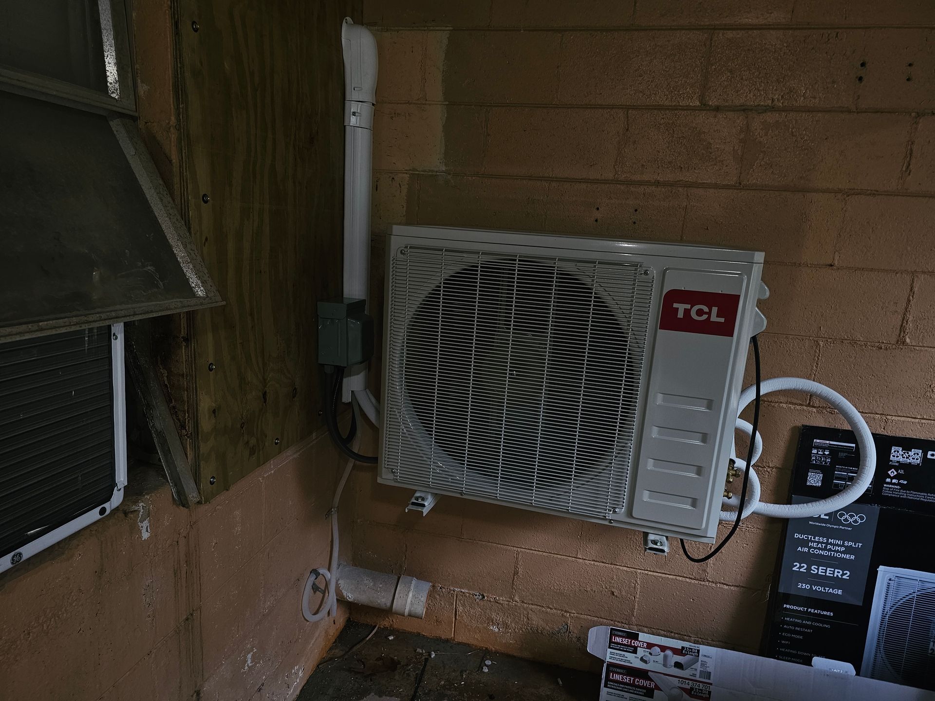 Window air conditioner mounted in a brick wall, with power cord and nearby window screen.