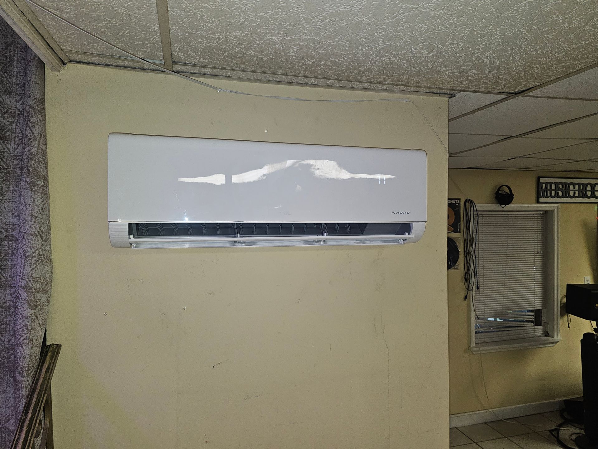 White wall-mounted air conditioner on a beige wall under a textured ceiling.