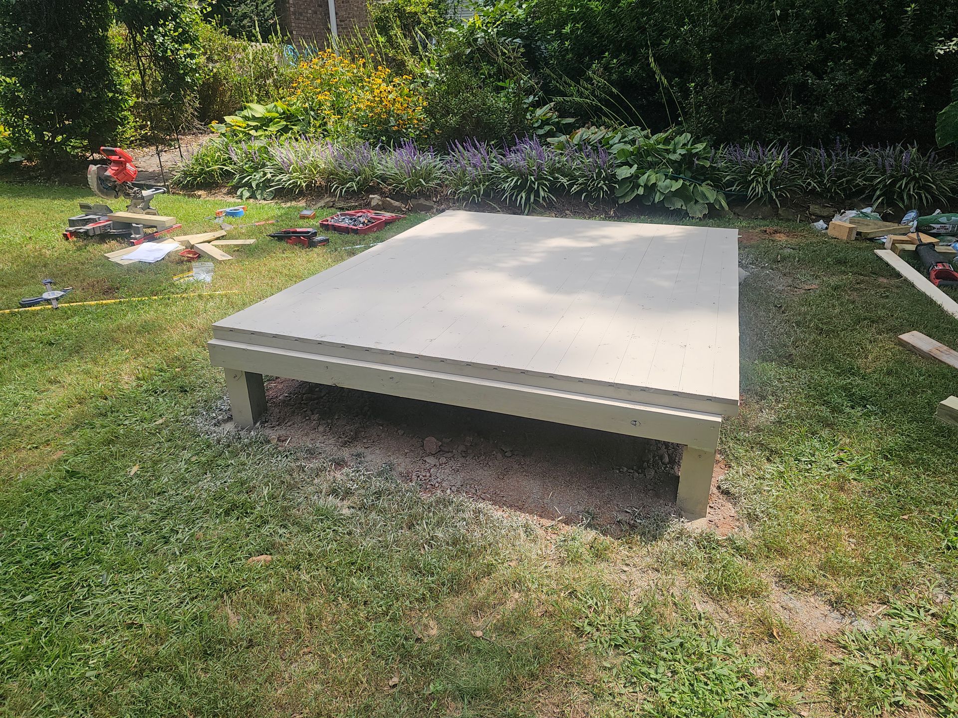 Raised concrete slab in a grassy backyard with garden beds and trees nearby.