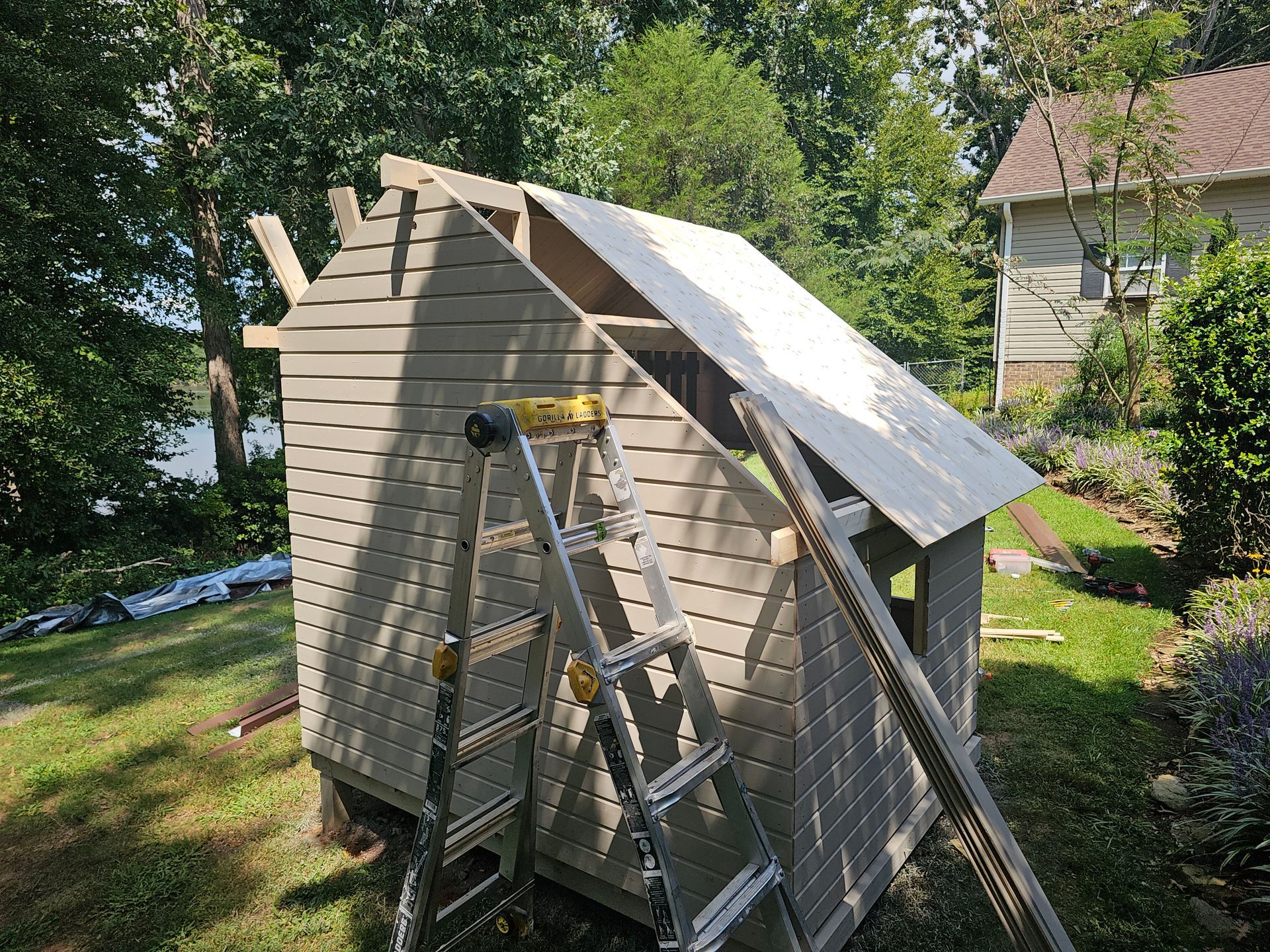 Small wooden shed under construction with ladders and boards in a grassy yard