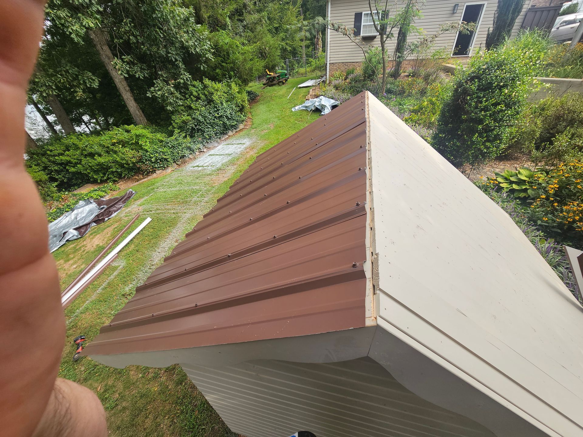 Brown and white roof edge on a house, viewed from above in a leafy yard