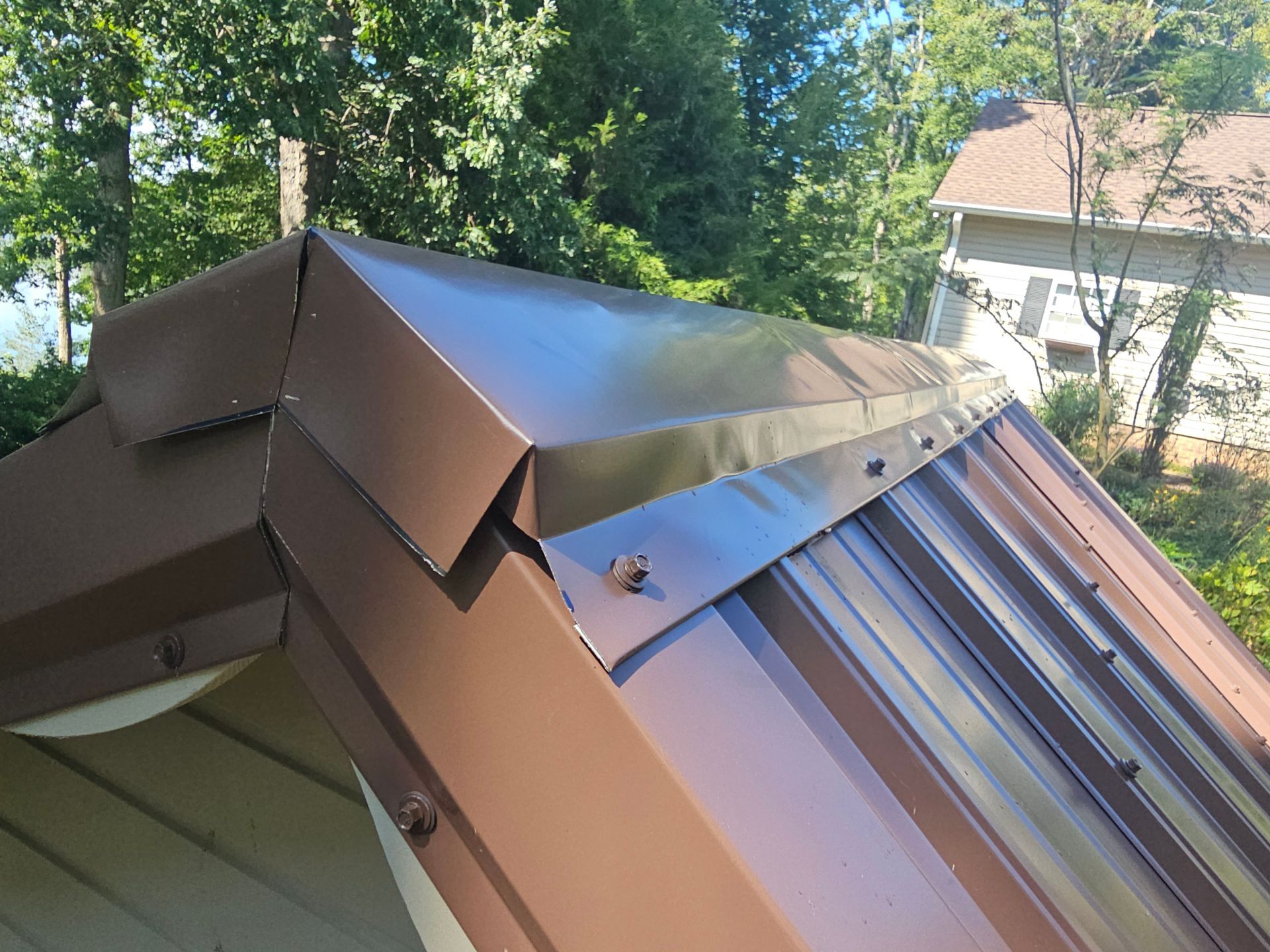 Brown metal roof flashing on a sloped roof, with trees and a house in the background