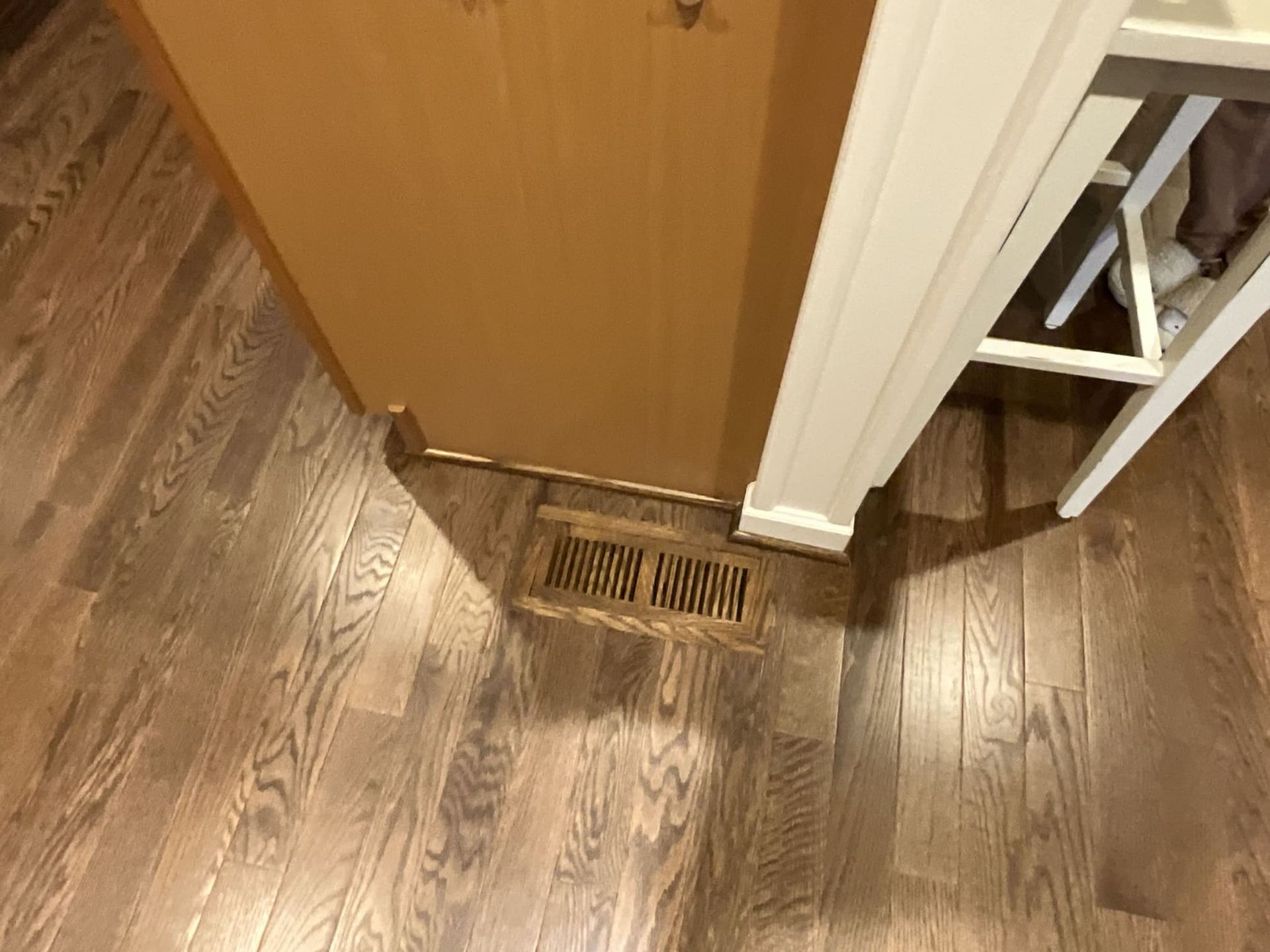 A wooden floor with a vent underneath it in a kitchen.