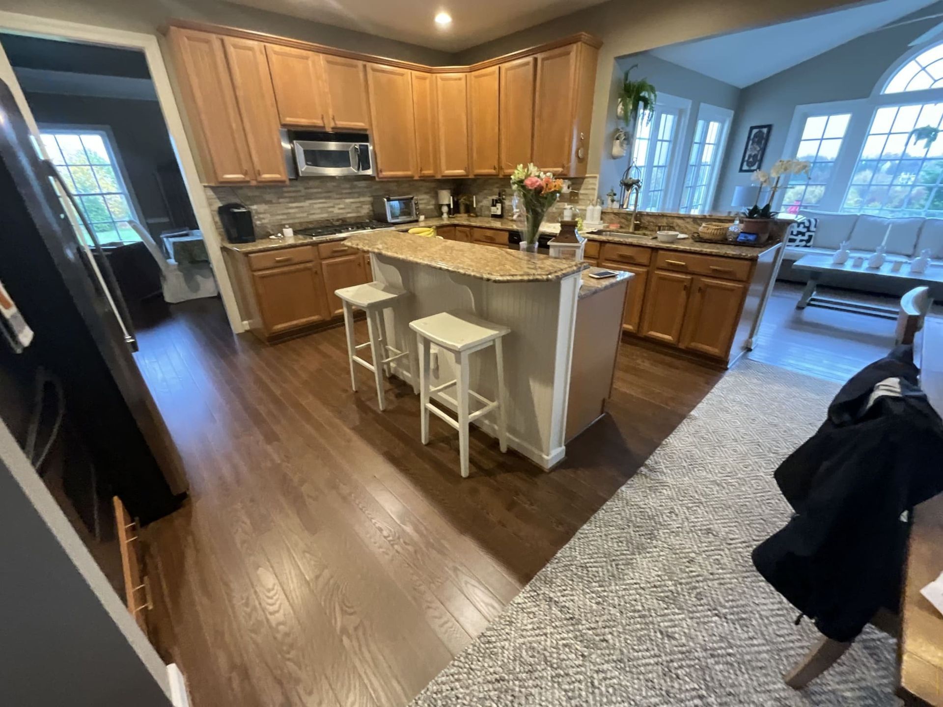 A kitchen with wooden cabinets , granite counter tops , stools and a refrigerator.