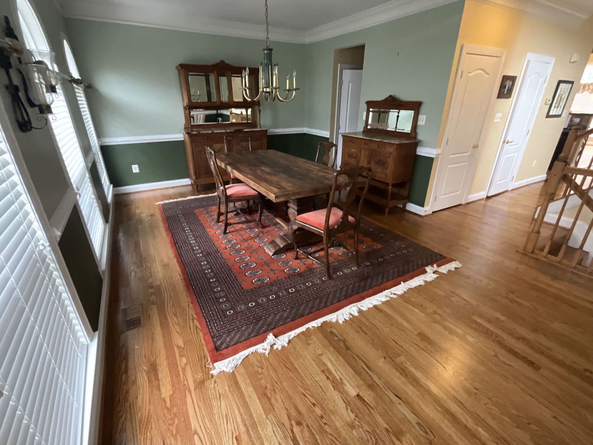 A dining room with a wooden table and chairs and a rug on the floor.