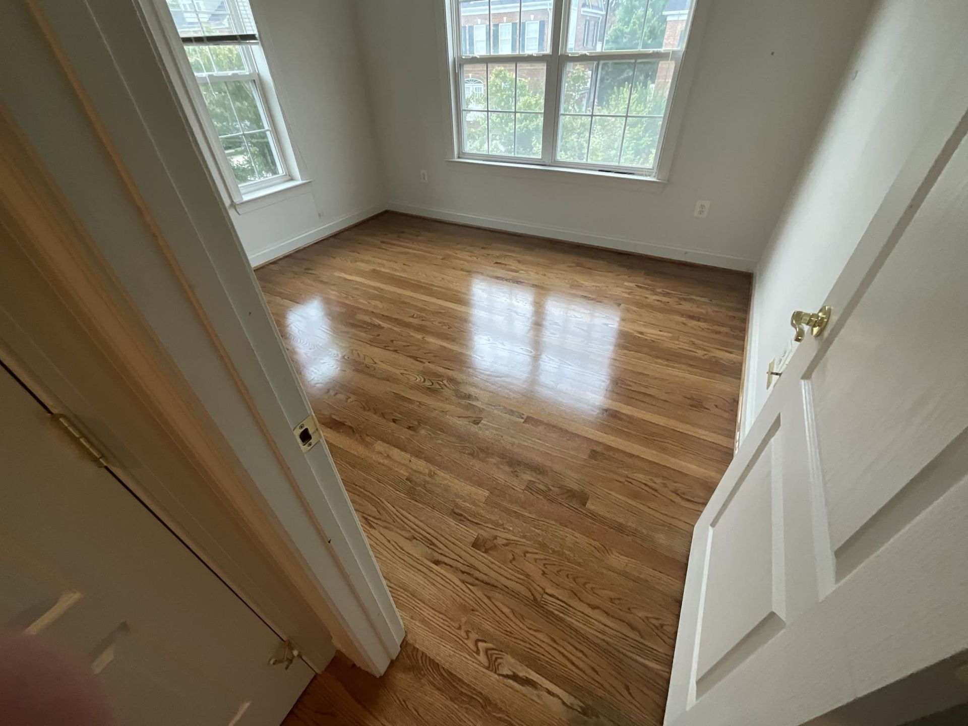 A bedroom with hardwood floors and two windows.