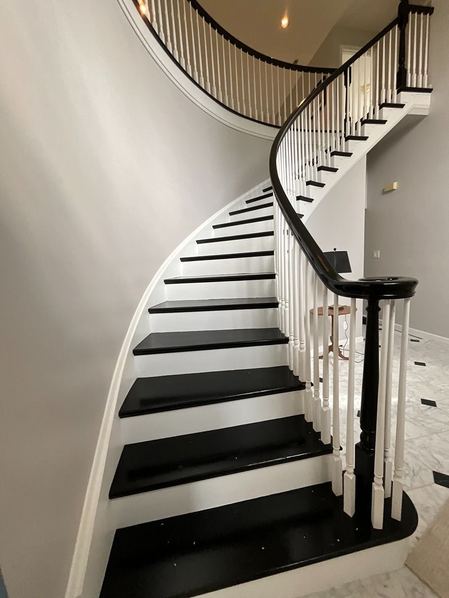 A curved staircase with black steps and a white railing
