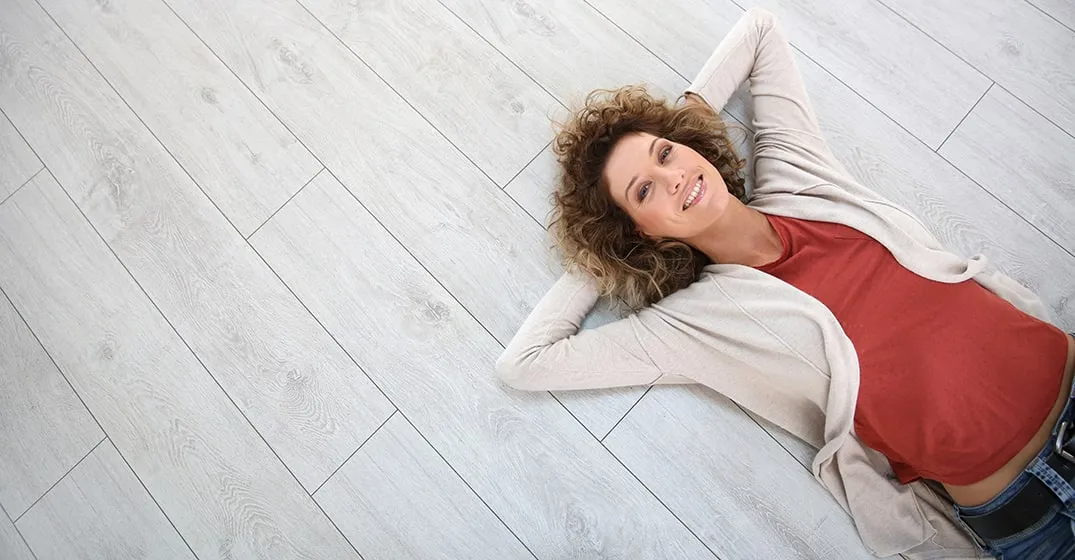 A woman is laying on the floor with her hands behind her head and smiling.