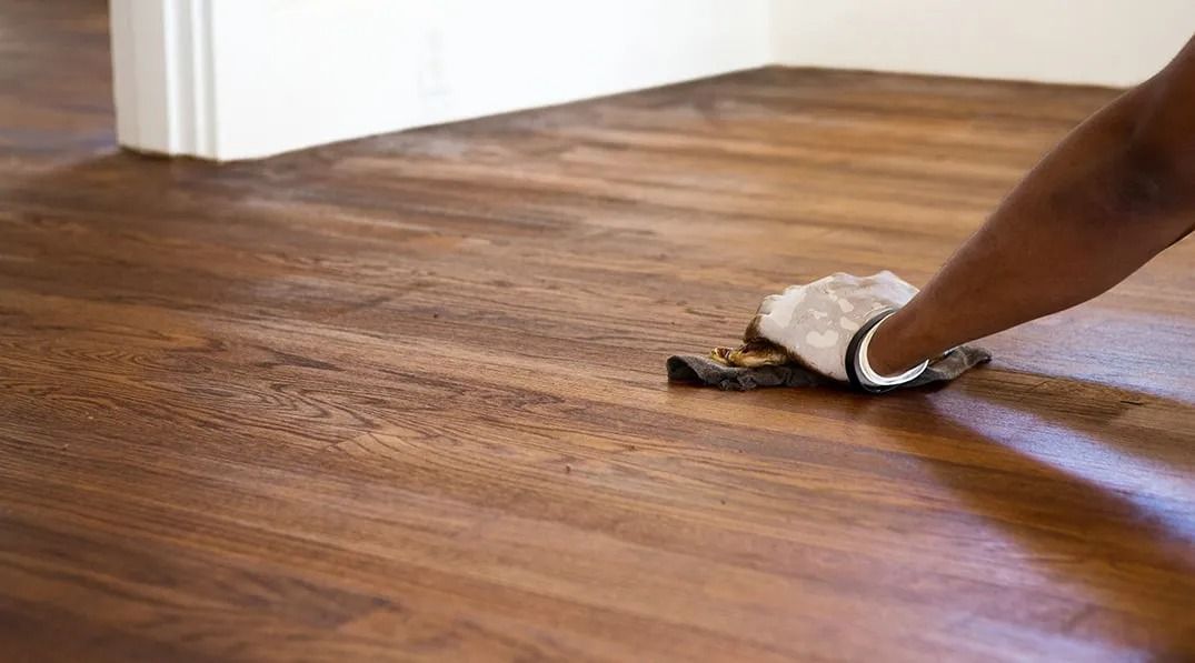 A person is cleaning a wooden floor with a cloth.
