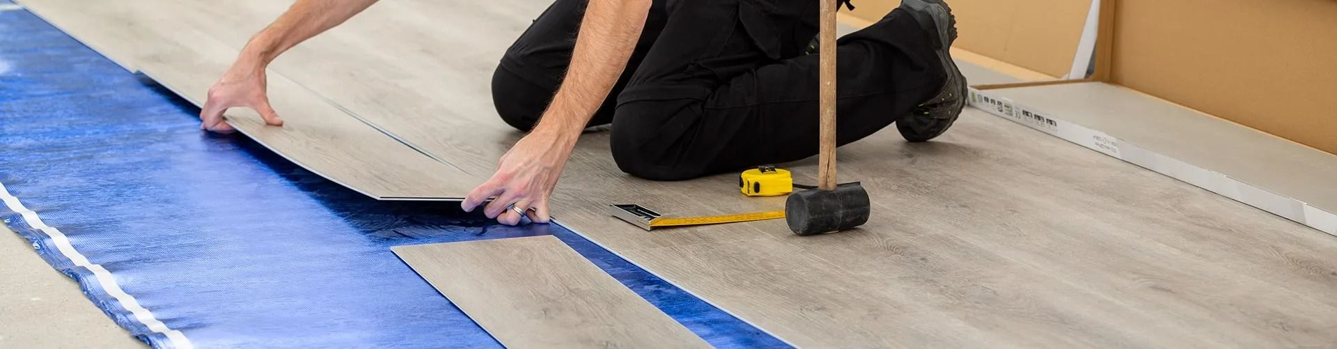 A person is kneeling down to install a hardwood floor.