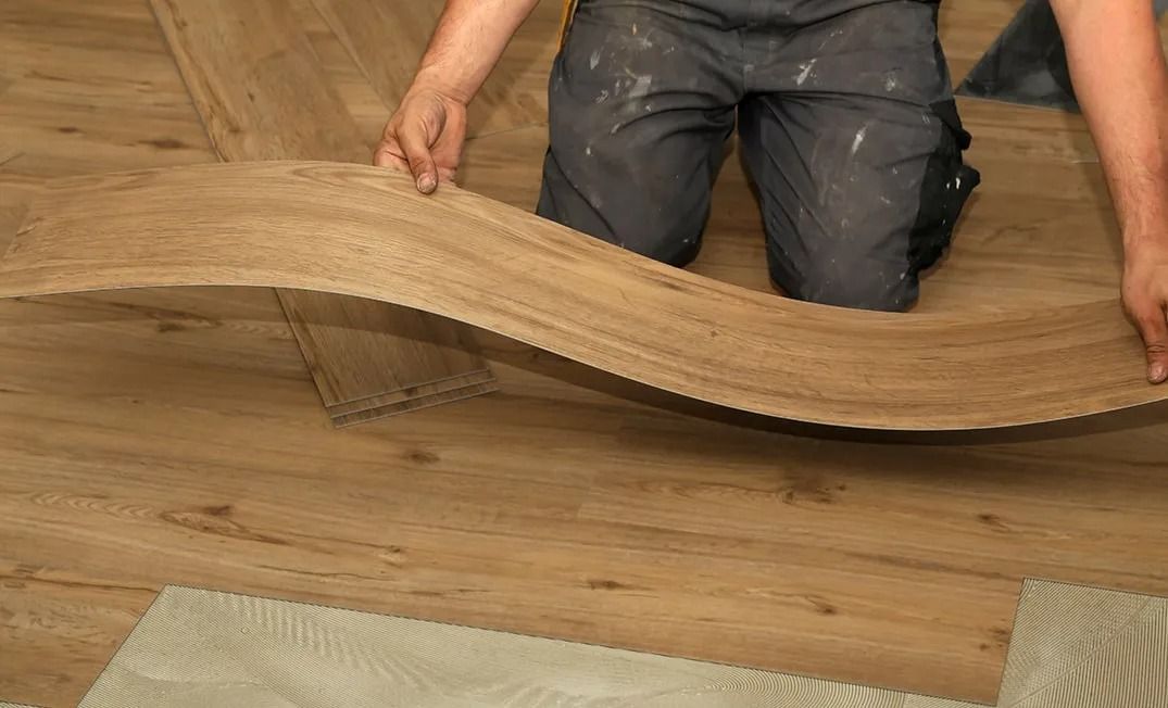 A man is kneeling down on the floor holding a piece of wood.