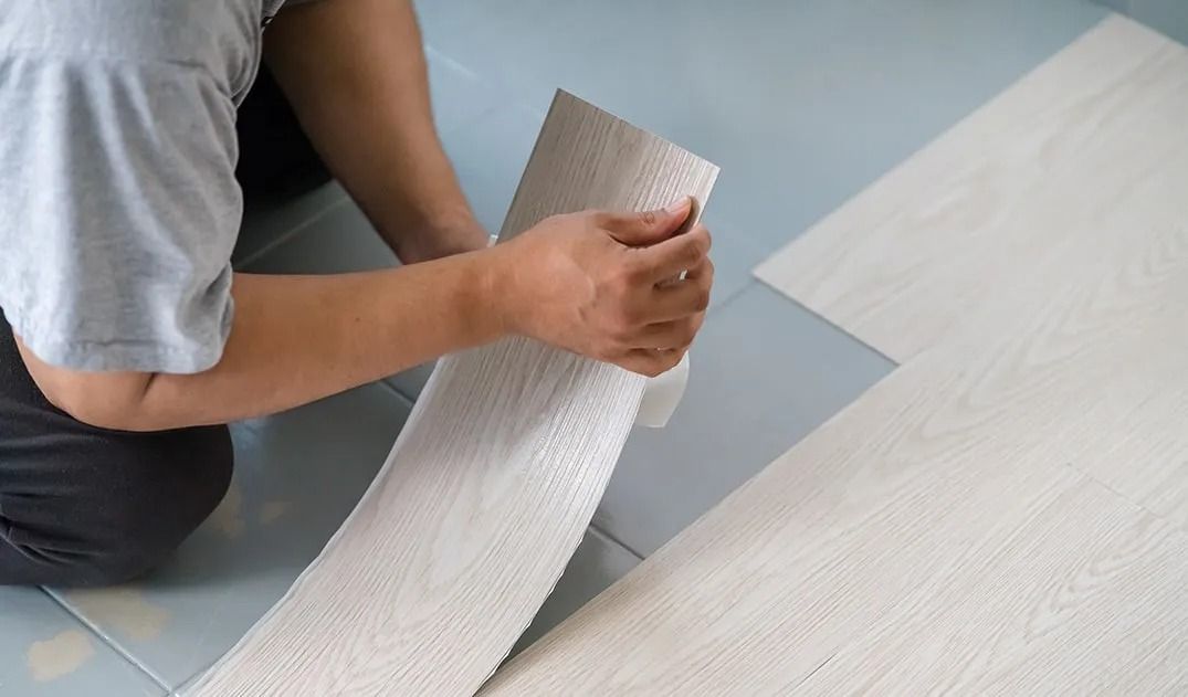 A person is laying a piece of vinyl flooring on the floor.